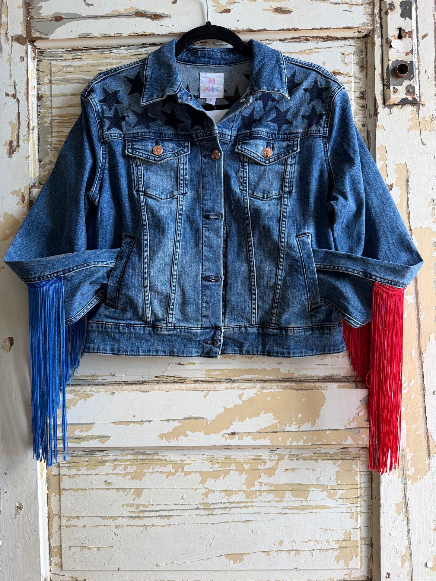 Blue denim jacket with red and blue fringes on a rustic wooden door