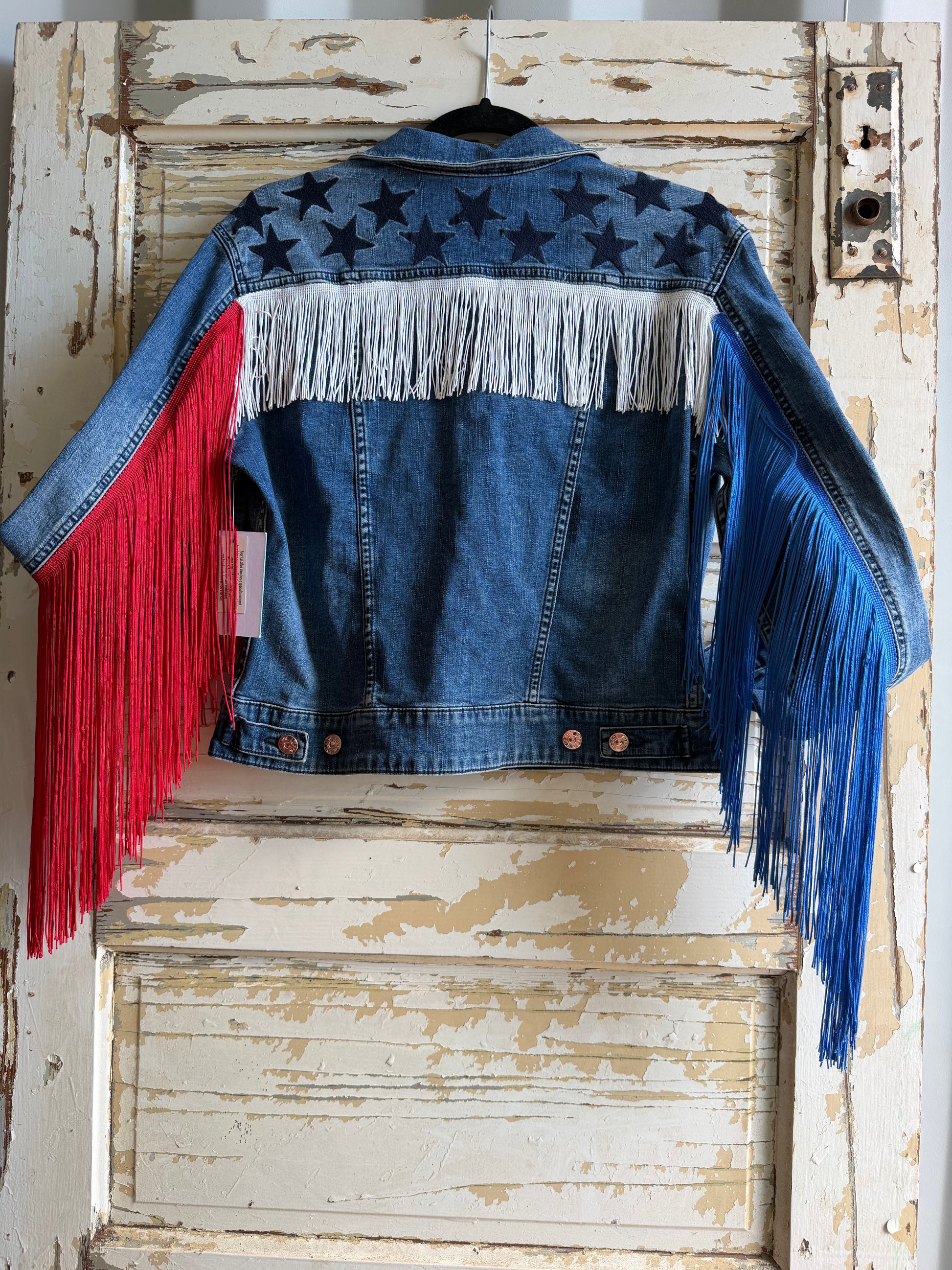 Denim jacket with colorful fringe on a rustic wooden door