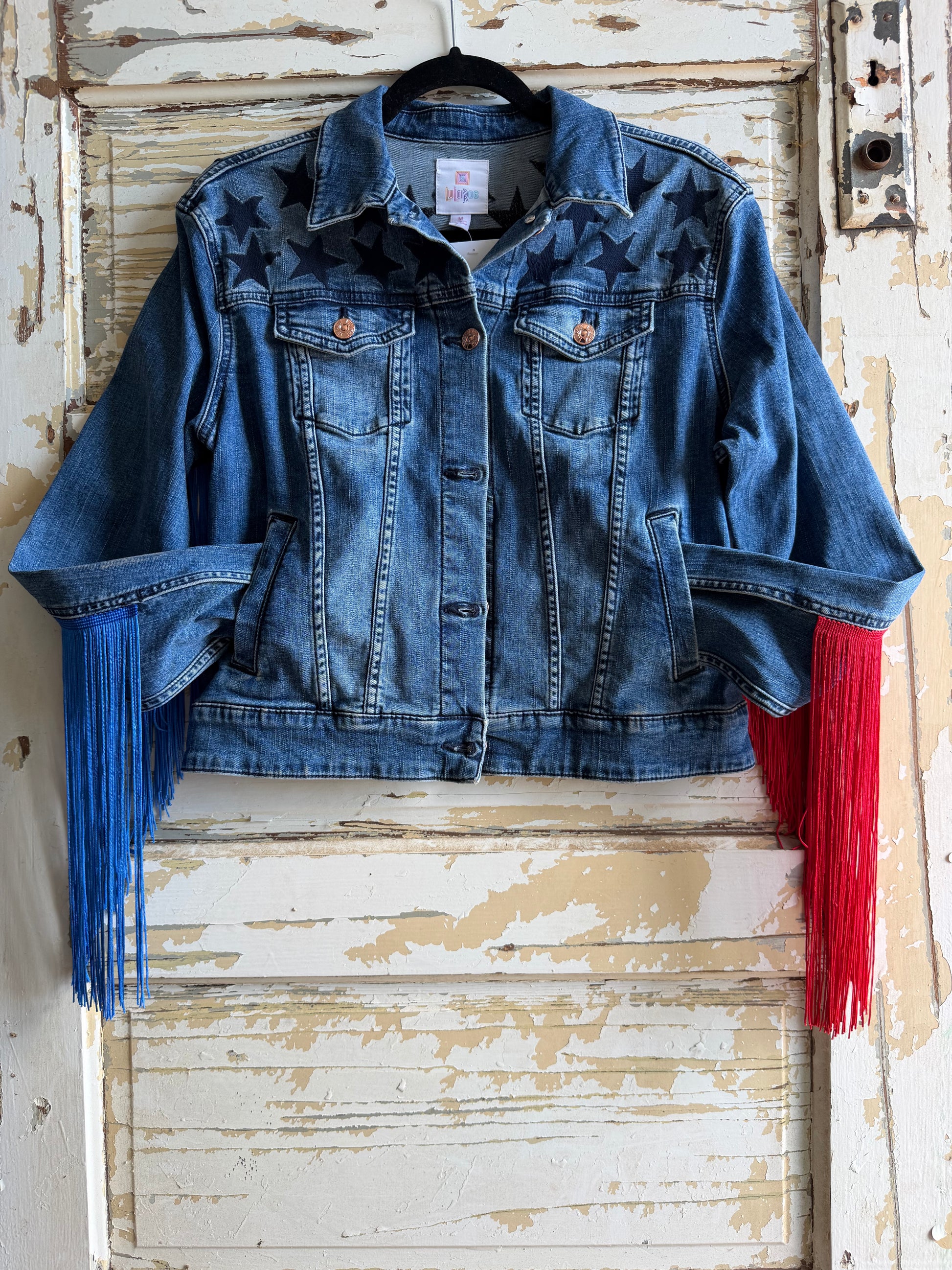 Blue denim jacket with red and blue fringes on a rustic wooden door